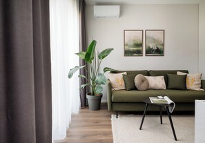 A modern living room with a green sofa, decorative pillows, a potted plant, and two framed artworks on the wall. - Wola Redutowa Superior Apartment (Warszawa)