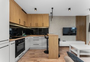 A modern kitchen with wooden cabinets, a black stove, and a bar area. - Sosnowiec Modern Apartment (Sosnowiec)