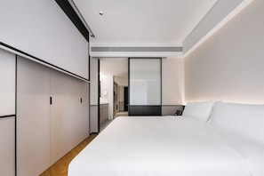 Una habitación de hotel moderna con una cama grande, un armario y un baño visible a través de una puerta.