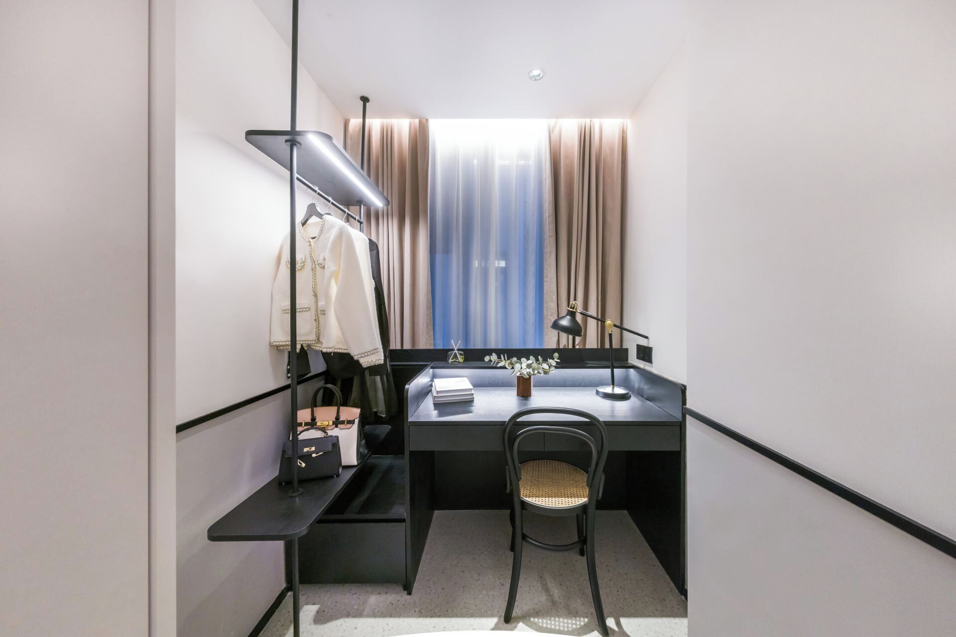 A compact hotel room with a desk, chair, and a wardrobe.