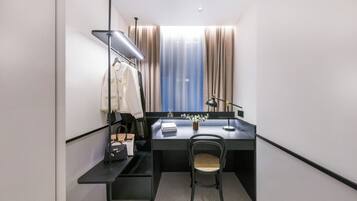 A compact hotel room with a desk, chair, and a wardrobe.