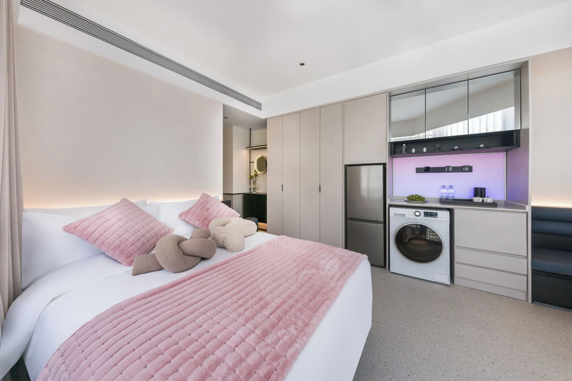 A modern hotel room with a bed, a washing machine, and a kitchenette.