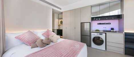 A modern hotel room with a bed, a washing machine, and a kitchenette.