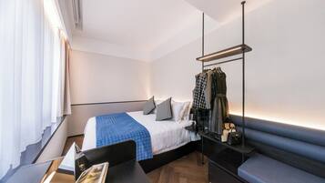 A modern hotel room with a bed, bedside table, and a clothing rack.