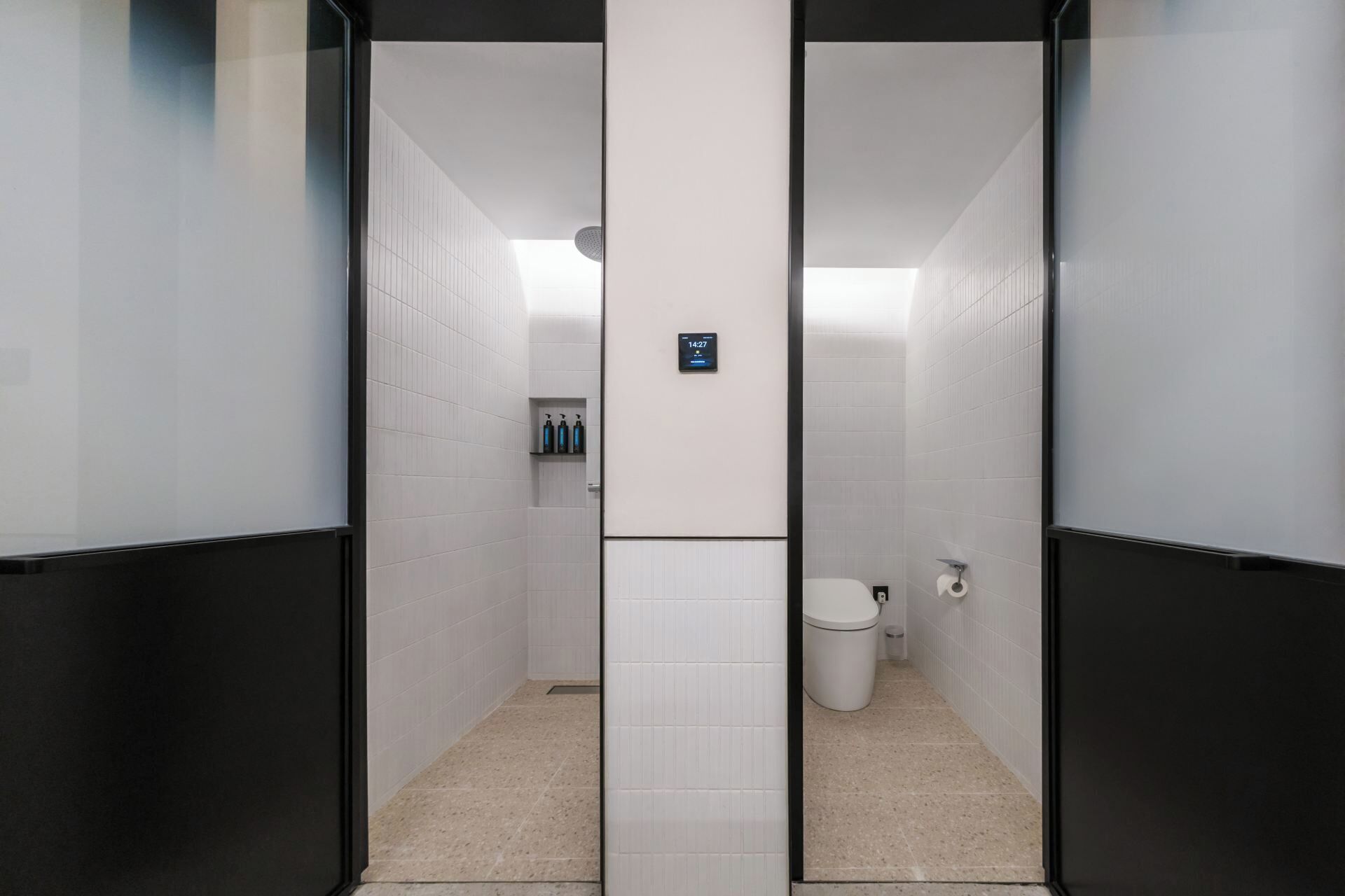 Ein modernes Badezimmer mit Glastrennwand, digitaler Uhr und Toilette.