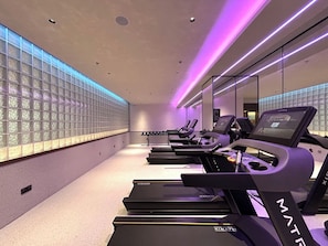 Un gimnasio con cintas de correr, paredes con espejos y un revestimiento de pared estampado.