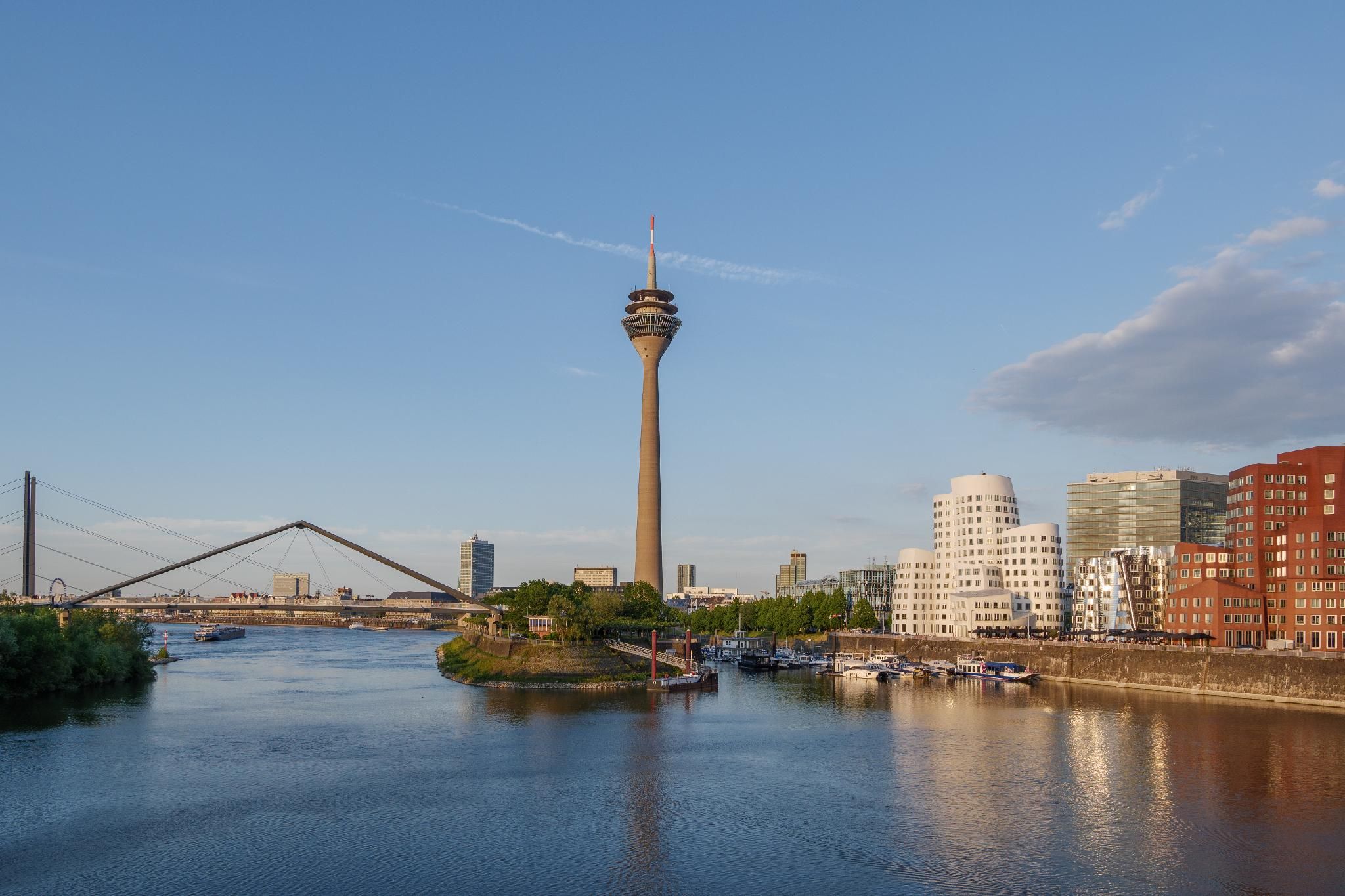 Eine Stadtansicht mit einem markanten Turm, einer Brücke und einem Fluss mit Booten.