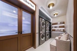 A laundry room with a wooden door, a washing machine, a dryer, and a seating area with cushions. - Shanghai Xujiahui Grow Suisse Place Apartment Hotel (Shanghai)