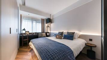 A modern bedroom with a large bed, bedside tables, a desk, and a chair.