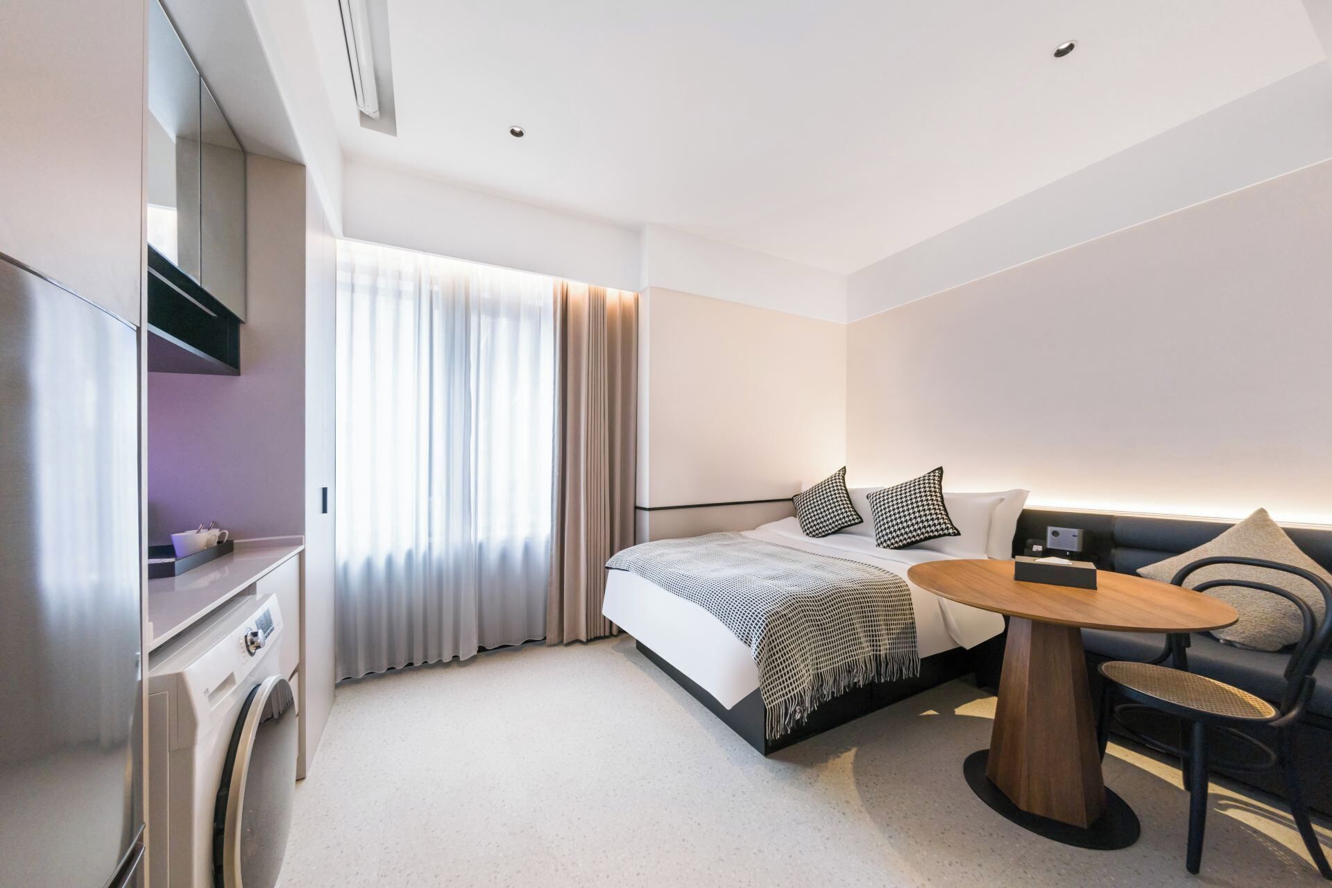 Moderni hotellihuone, jossa on sänky, työpöytä, tuoli ja pieni pöytä.