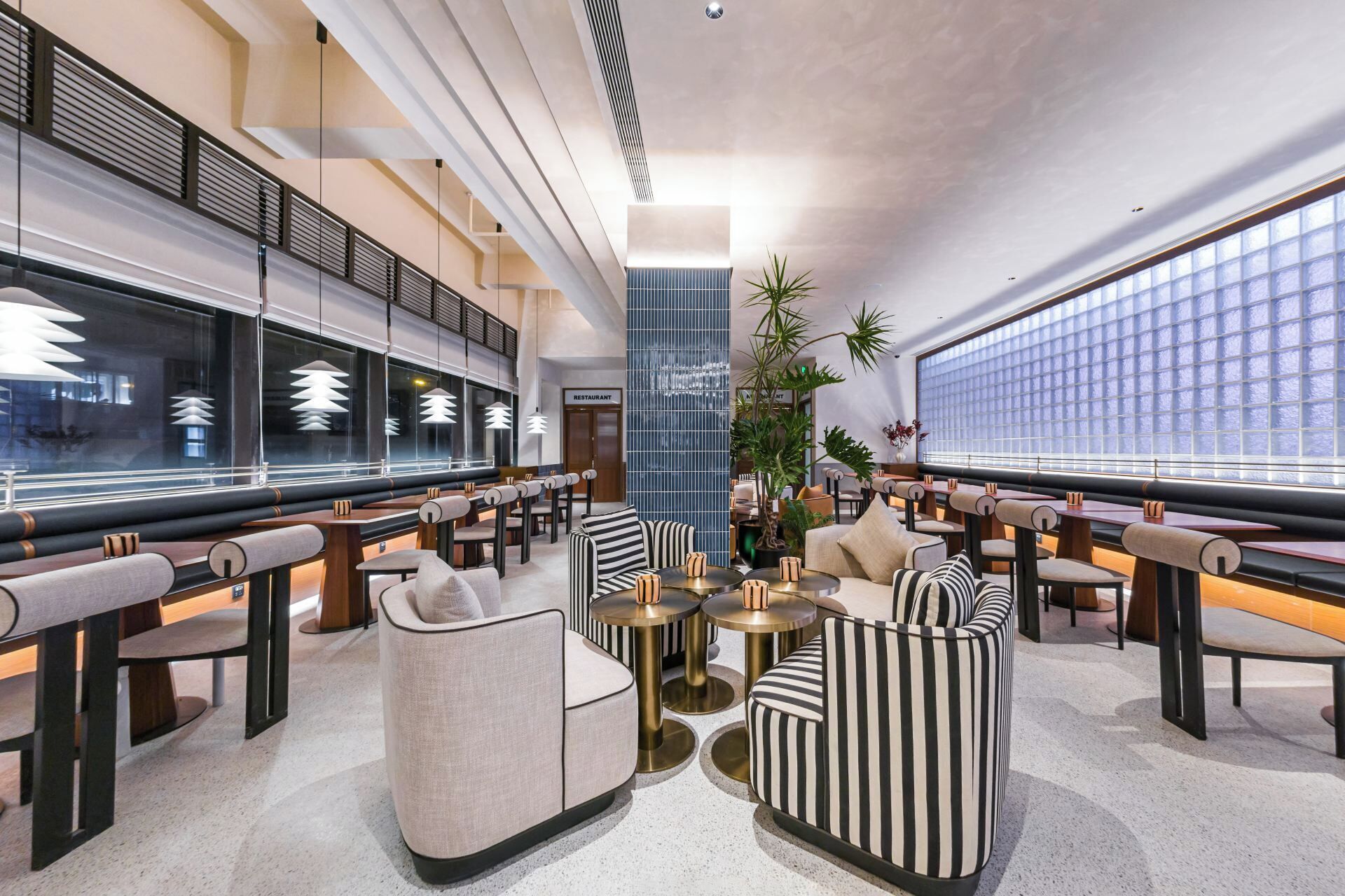 A modern lounge area with seating arrangements, a central plant, and a large window providing natural light.