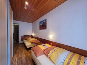 A hotel room with wooden flooring, a bed with a patterned bedspread, a wall-mounted picture, and a ceiling light. - Am Biel 2 by Interhome (Saas-Fee)