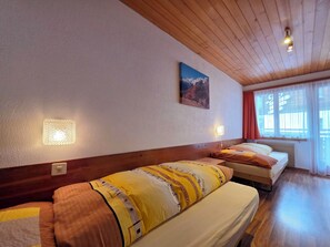 Ein Hotelzimmer mit zwei Betten, einer Holzbalkendecke, einem Gebirge auf der Wand und einem Fenster mit Vorhängen.
