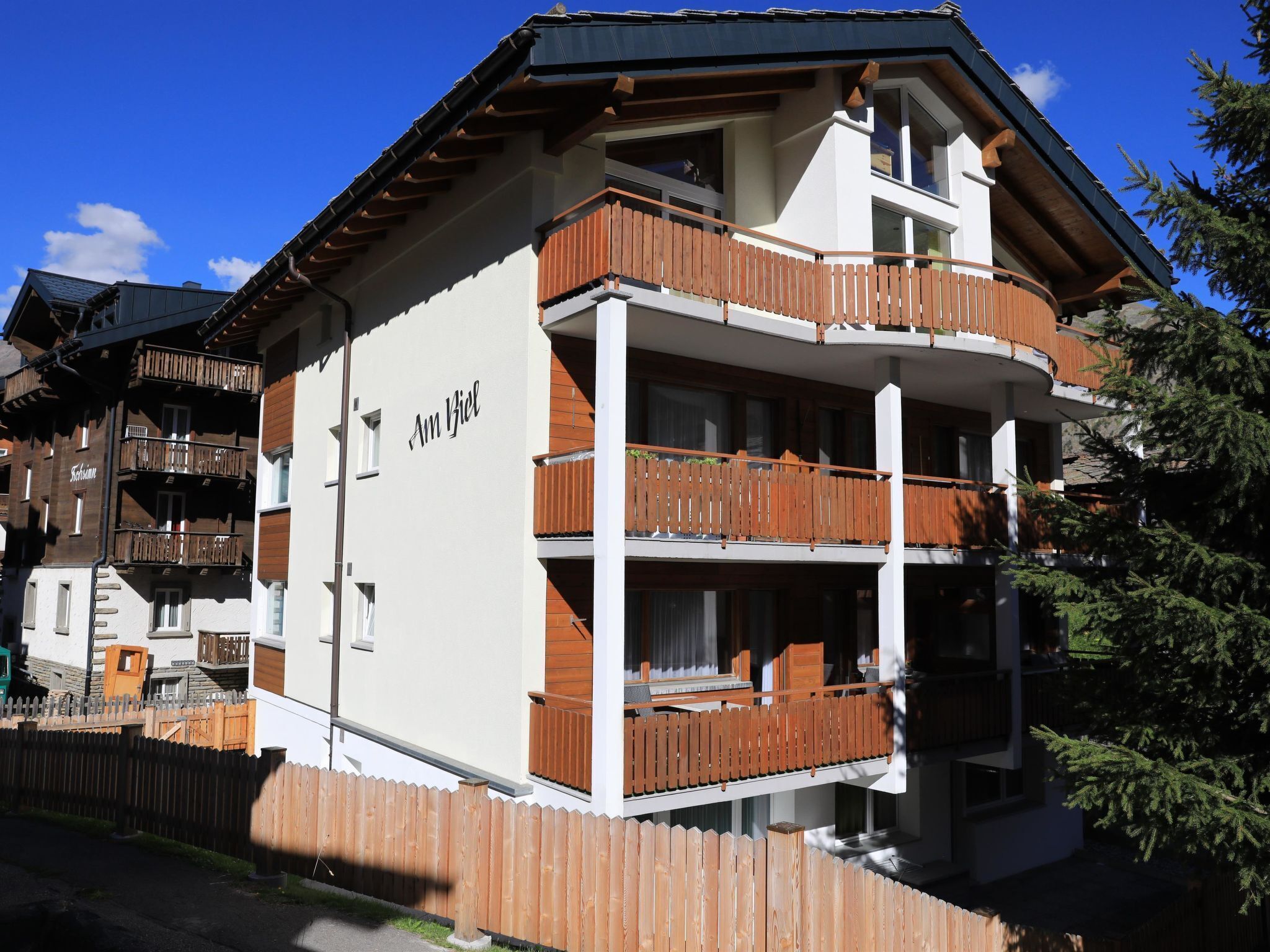 Un immeuble à plusieurs étages, doté d’un balcon en bois au deuxième étage, d’une enseigne indiquant « Am Biel » et d’une façade blanche.