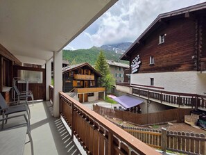 Ein Balkon mit Bergblick, ein Holzhaus mit einem Schild und ein eingezäunter Außenbereich.