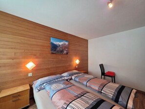 Une chambre avec deux lits, des lambris en bois aux murs, un tableau représentant un paysage de montagne et deux lampes fixées au mur.