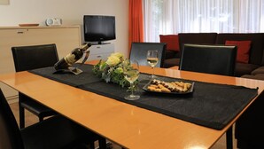 Uma mesa de jantar com uma garrafa, copos e um prato de comida em um quarto com televisão e sofá.
