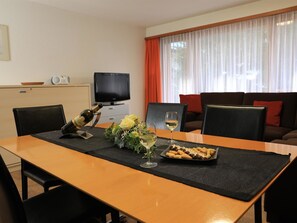 Ein Esstisch mit einer Flasche, Gläsern und einem Teller mit Essen in einem Raum mit Fernseher und Sofa.