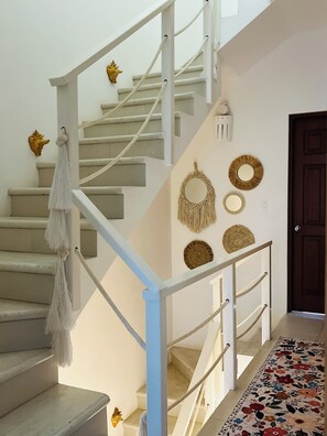 A staircase with white railings, a white wall with decorative wall hangings, and a patterned carpet. - OTOMI HOUSE, PUERTO MORELOS (Puerto Morelos)