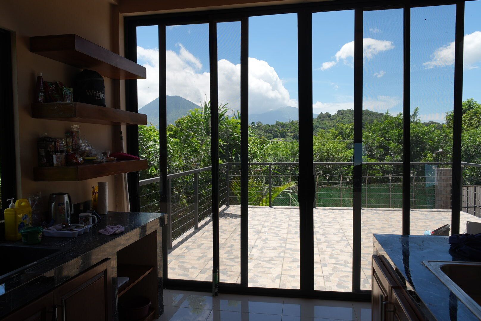A kitchen with a view of a balcony, outdoor area, and a mountain in the distance.