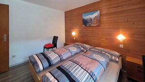 Ein Schlafzimmer mit Holzpaneelen, einem Bett mit gestreifter Bettwäsche, einem Stuhl und zwei Wandleuchten.