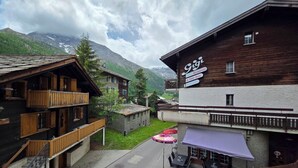 Ein Bergdorf mit traditionellen Holzhäusern, einem Restaurant namens 'Gigi' und Blick auf schneebedeckte Berge.
