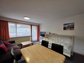 Um quarto com sofá, mesa de madeira, cama, televisão e um quadro na parede.