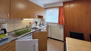 Eine kleine Küche mit Holzausstattung, einem Einbauofen, einem Spülbecken und einem Fenster mit Vorhängen.