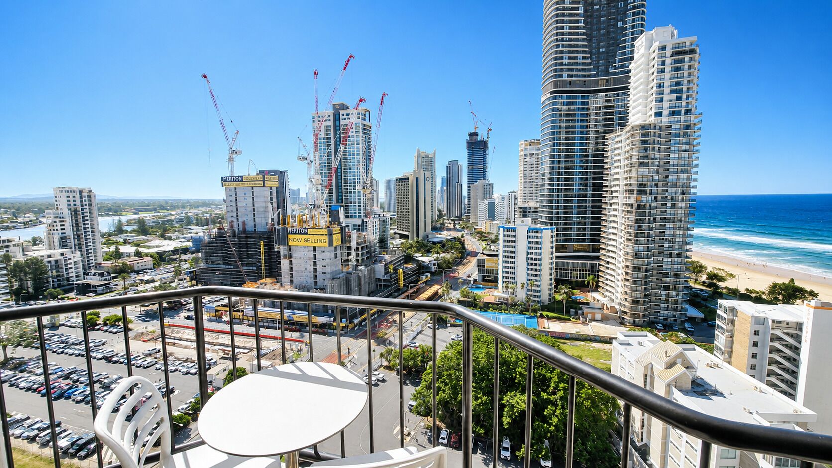 A cityscape with high-rise buildings, a beach, and a balcony with a table and chairs.