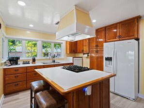 Une cuisine moderne avec des meubles en bois, un îlot central, une cuisinière encastrée et un réfrigérateur.
