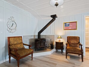 Une pièce avec un poêle à bois, deux fauteuils richement décorés, une horloge murale et un drapeau américain encadré.