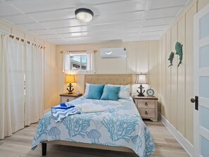 Une chambre à coucher comprenant un lit, des tables de chevet, une fenêtre, un appareil de climatisation et une porte.