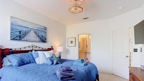 Une chambre à coucher avec un lit, une table de chevet, une lampe, une étoile de mer en guise de décoration, un tableau, une porte et une commode.