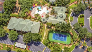 Vue aérienne d’un complexe hôtelier comprenant plusieurs bâtiments, une piscine, des courts de tennis et des aires de stationnement.