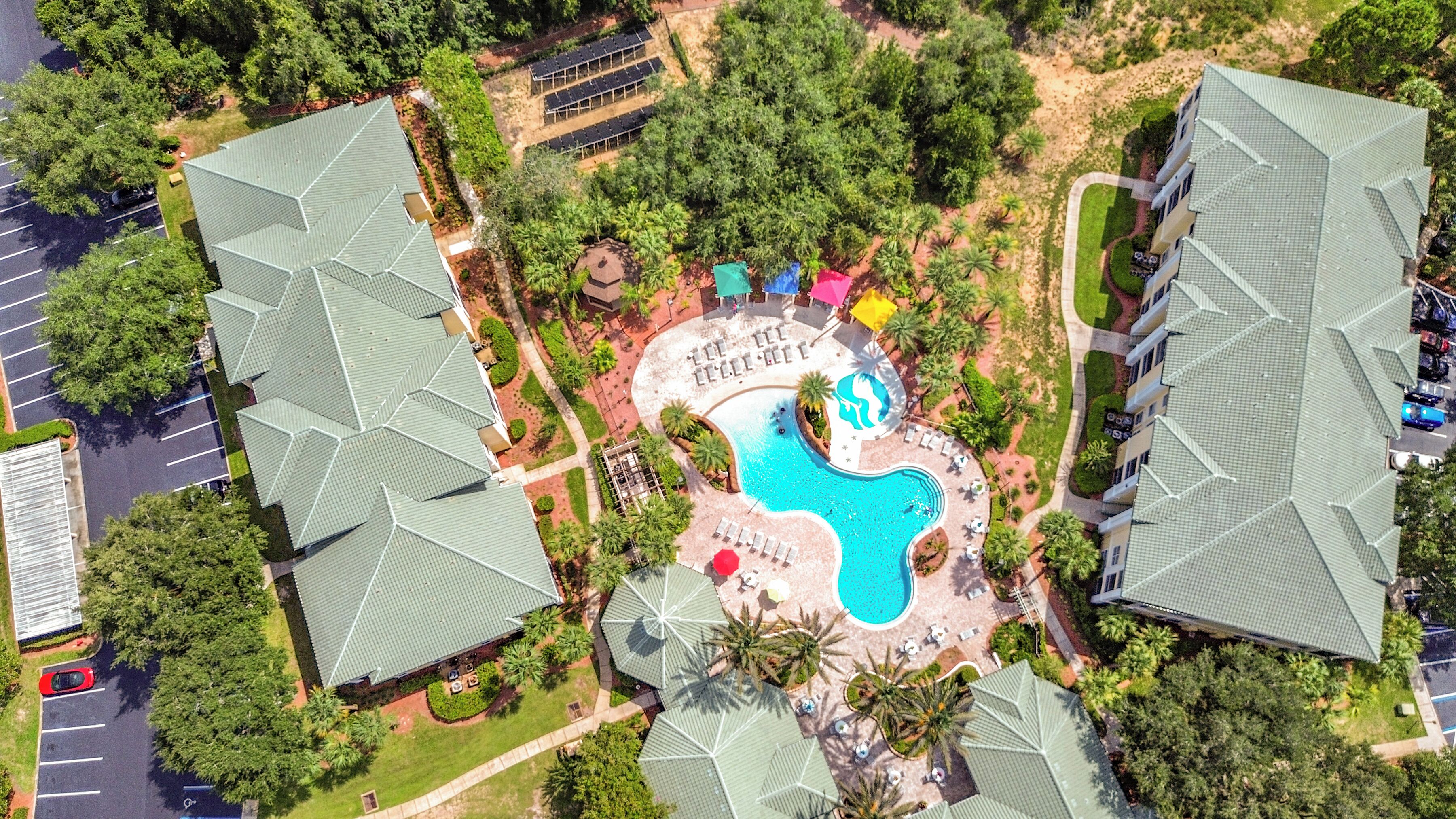 Vue aérienne d’un hôtel avec une piscine, des chaises longues et un parking.