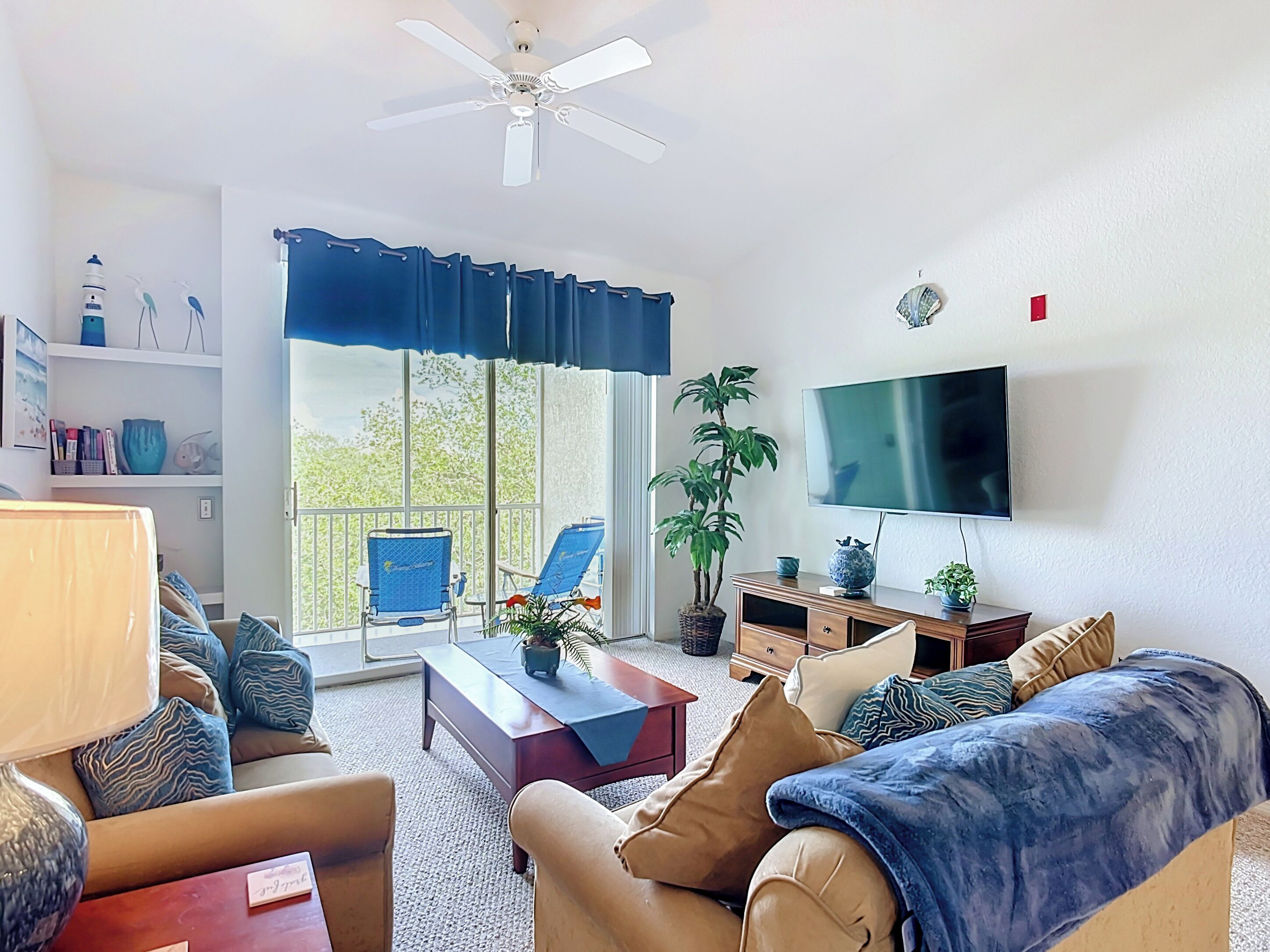 A living room with a sofa, armchairs, a coffee table, a TV, and a balcony with blue curtains.