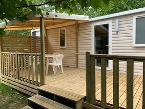 A wooden deck with a covered seating area, a window, and a door. - Mobile home with a patio and the campground's pool (Ouistreham)