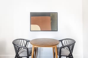 A dining area with a round wooden table and two black chairs with cushioned seats. - Blueground | Bloomingdale, gym, nr Riverside Park (New York)