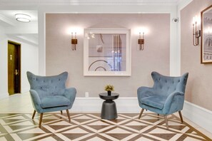 A modern lobby with two blue armchairs, a geometric patterned floor, a framed abstract painting, and wall sconces. - Blueground | Bloomingdale, gym, nr Riverside Park (New York)