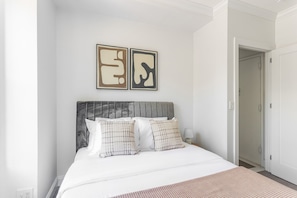 A bedroom with a bed, pillows, a headboard, and two wall art pieces. - Blueground | Bloomingdale, gym, nr Riverside Park (New York)