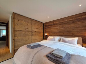 Un dormitorio moderno con cabecera de madera, cama con ropa de cama blanca y vistas al exterior.