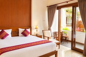 A hotel room with a large bed, a wooden headboard, a nightstand with a lamp, a chair, and a table with potted plants. - Delux Room resort in fabulous Kedewatan Ubud (Kedewatan ubud)