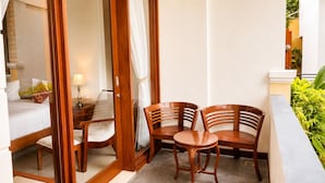 Een hotelkamer met een bed, een nachtkastje met lamp, een houten stoel, een klein rond tafeltje en een gordijn.