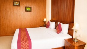 Ein Hotelzimmer mit einem Holz-Kopfteil, einem Bett mit weißer Bettwäsche und roten Akzenten, zwei Nachttischlampen und zwei gerahmten Bildern an der Wand.