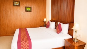 A hotel room with a wooden headboard, a bed with white bedding and red accents, two bedside lamps, and two framed pictures on the wall. - Delux Room resort in fabulous Kedewatan Ubud (Kedewatan ubud)