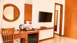 Een hotelkamer met een houten bureau, een televisie, een koffiezetapparaat en een minibar.