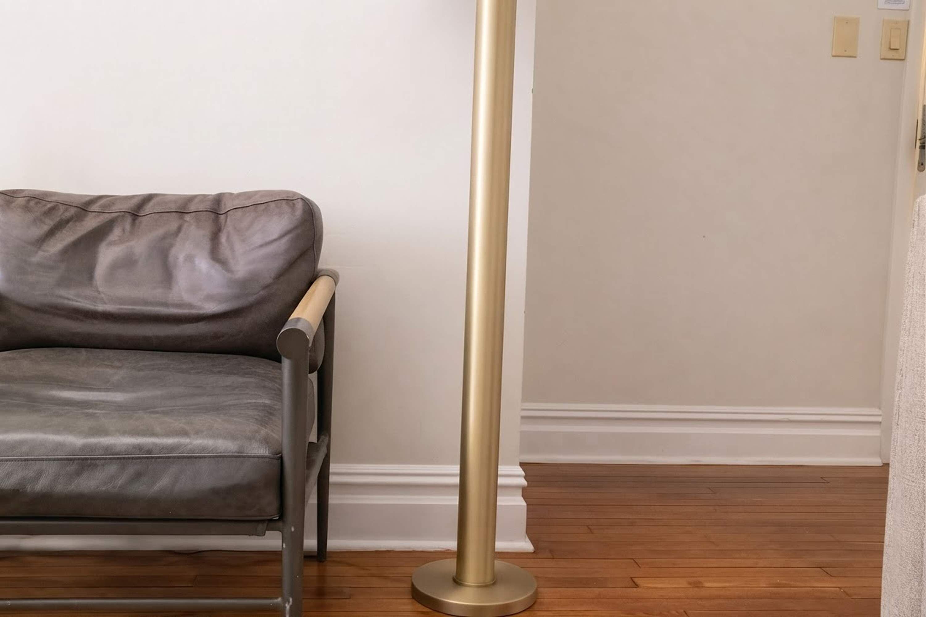A room with a leather sofa, a tall floor lamp, wooden flooring, and white walls.