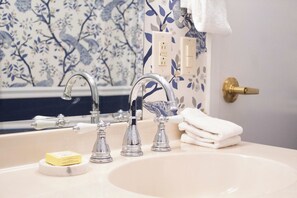 A bathroom with a sink, two faucets, a towel, and a soap dish. - Queen Double Room | StayCozy at The Arco (Philadelphia)
