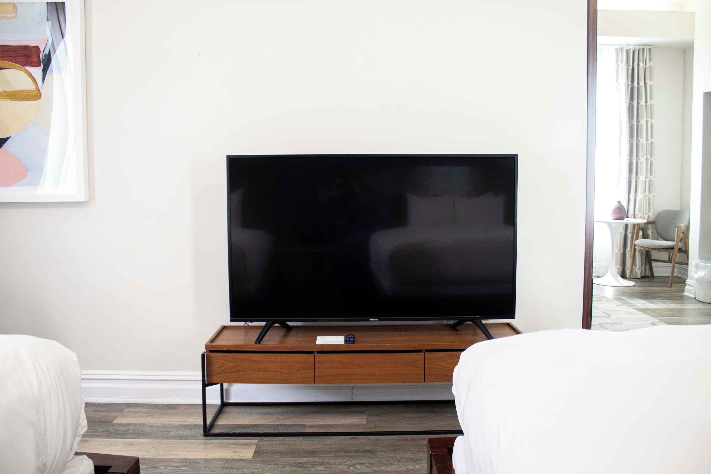 A modern living room with a flat-screen TV on a wooden stand, two white sofas, and a painting on the wall.