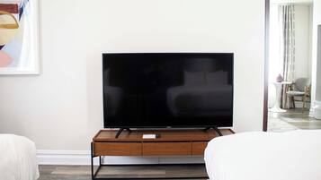 A modern living room with a flat-screen TV on a wooden stand, two white sofas, and a painting on the wall.
